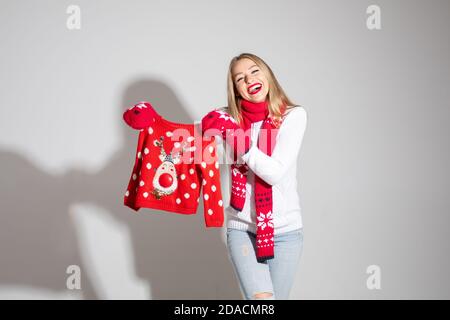 Attraktive Frau in weißem Pullover, rotem Schal und roten Fäustlingen mit weihnachts-Design hält roten Pullover Stockfoto