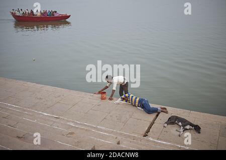 Varanasi, Indien, November 2015. Ein Mann, der ein Ghat des Ganges malt, während ein Mann und ein Hund schlafen. Stockfoto