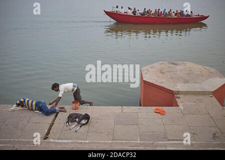 Varanasi, Indien, November 2015. Ein Mann, der ein Ghat des Ganges malt, während ein Mann und ein Hund schlafen. Stockfoto