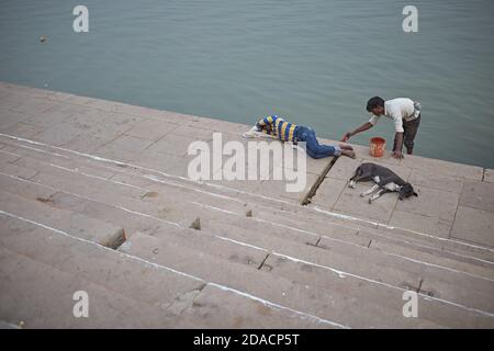 Varanasi, Indien, November 2015. Ein Mann, der ein Ghat des Ganges malt, während ein Mann und ein Hund schlafen. Stockfoto