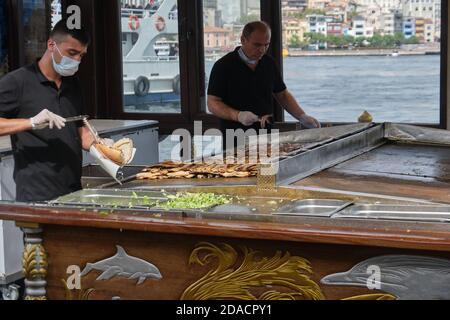 Personal mit Gesichtsmasken Kochen Balik Ekmek auf einem Boot in Eminonu Hafen, Istanbul, Türkei Stockfoto