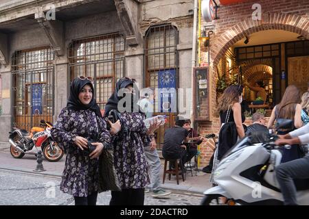 Zwei türkische Schwestern in identischer Kleidung und Sonnenbrille und mit einer Gesichtsmaske, die in den trendigen Sitzen von Balat, Istanbul, Türkei, spazieren geht Stockfoto