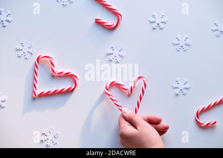 Herzformen aus Bonbonstöcken, rot weiß gepunktete Schmuckstücke auf weißem Textil. Hand halten Herz. Stockfoto