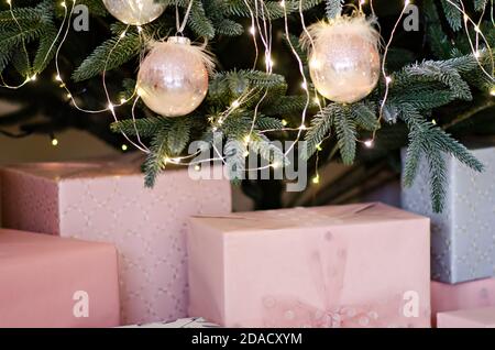 Viele Geschenke in rosa und grauem Papier eingewickelt, verziert mit Luftbändern mit einer Schleife, Girlanden unter dem Weihnachtsbaum vom Weihnachtsmann. Neujahrskarte Stockfoto