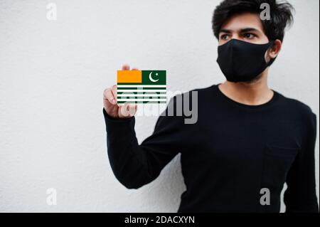 Asian Mann tragen ganz schwarz mit Gesichtsmaske halten Azad Kaschmir Flagge in der Hand isoliert auf weißem Hintergrund. Coronavirus-Länderkonzept. Stockfoto