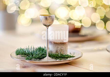 Grußkarte zum neuen Jahr. Auf dem Holztisch befindet sich eine graue Tasse heißer Schokolade, verziert mit einem Christbaumzweig. Verwackelte helle gelbe Lichter Bokeh Stockfoto