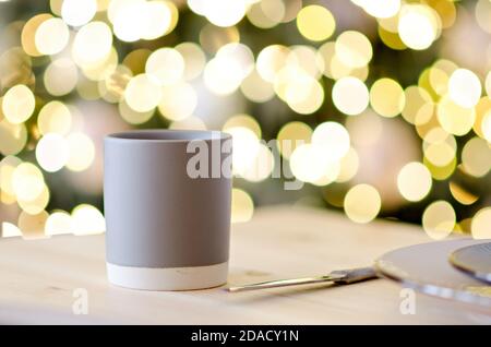 Grußkarte zum neuen Jahr. Auf dem Holztisch befindet sich eine graue Tasse heißer Schokolade, verziert mit einem Christbaumzweig. Verwackelte helle gelbe Lichter Bokeh Stockfoto