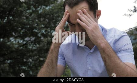 Angespannter Casual Mann mit Kopfschmerzen sitzt außerhalb Gebäude Stockfoto