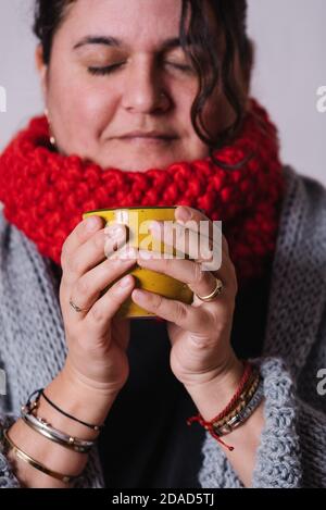 Vertikales Portraitbild einer Frau, die ihre Hände mit einem gelben Becher mit heißem Tee wärmt. Frau genießt die Wärme, die durch eine Tasse Tee erzeugt wird. Winter-Kontra Stockfoto