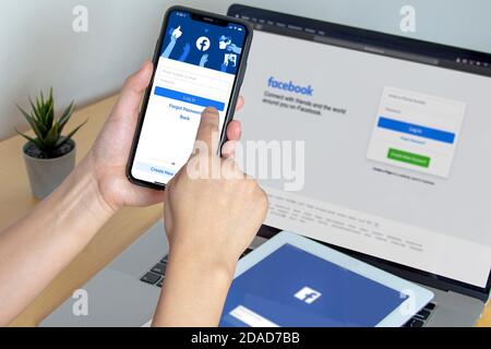 Calgary, Alberta. Kanada. November 11 2020: Eine Person, die die Facebook-App auf einem iPhone Pro 12, iPad und einem Macbook Pro auf einem Holztisch nutzt. Stockfoto