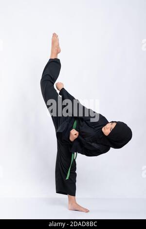 Frau in Hijab in pencak silat Uniform stellt eine gerade Kreisförmige Bewegung nach oben tritt auf einem isolierten Hintergrund Stockfoto