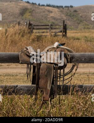 Ein alter, aus Leder gearbeitete Westernreitsattel auf einem Ranchzaun in Idaho. Jetzt Teil eines privaten Museums. Stockfoto