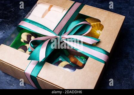 Box mit Satinbändern und leckeren Leckereien für Neujahr und Weihnachten. Neujahrsdesserts auf dunklem Hintergrund. Inhalte für das neue Jahr Stockfoto
