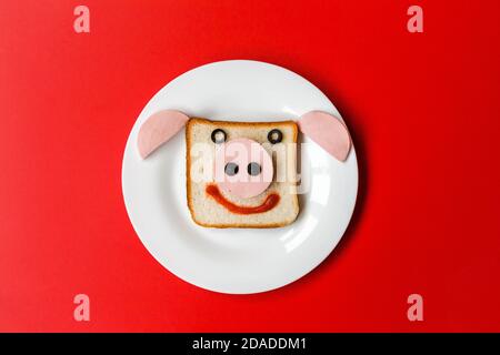 Ein Sandwich in Form eines Stierkopfes auf einem weißen Teller. Platte steht auf rotem Hintergrund Stockfoto