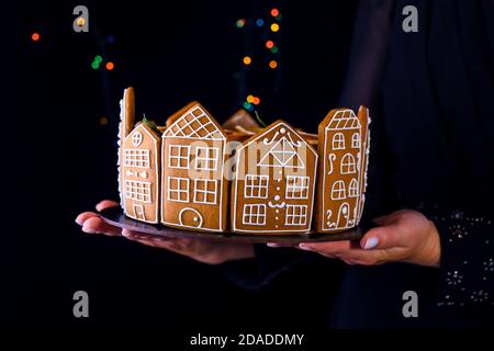 Ein Mädchen hält einen Weihnachtskuchen mit Lebkuchenhäusern. Ein Geburtstagskuchen. Urlaubsinhalt. Stockfoto