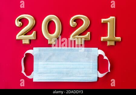Blaue medizinische Maske auf rotem Hintergrund und goldene Zahlen 2021 als Symbol des kommenden Jahres Stockfoto