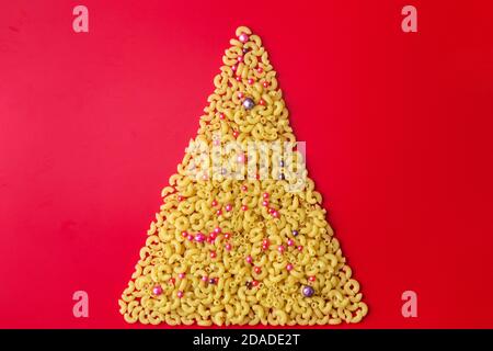 Weihnachtsbaum aus Pasta mit Kugeln auf rotem Hintergrund verziert Stockfoto