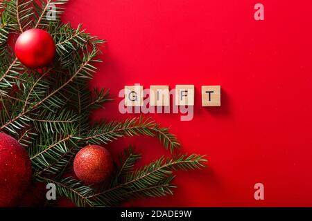 Weihnachtsbäume mit roten Kugeln und das WORTGESCHENK aus Holzbuchstaben auf rotem Hintergrund. Draufsicht. Saisonaler Verkauf. Stockfoto