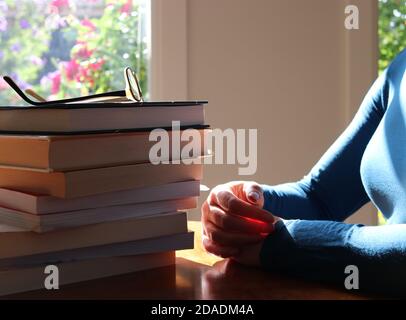 Frau mit Brille sitzt am Tisch mit einem Stapel Von Büchern Stockfoto