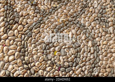 Hintergrund Textur von ausgebreitet Mosaik Kieselsteine. Die Textur der Steinmauer, die Straße aus kleinen runden und ovalen Steinen mit abstrakten Linien ausgelegt p Stockfoto