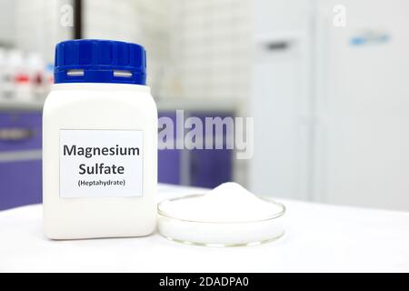 Selektiver Fokus von Magnesiumsulfat oder epsom Salz chemische Verbindung Flasche neben einer Petrischale mit weißem kristallinem Pulver im Chemielabor. Stockfoto