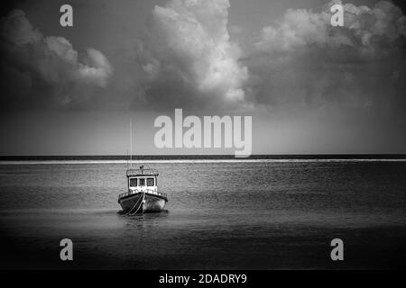 Einsames Motorboot am Strand. Dramatisches Meer in schwarz-weißen Farben, Horizont und wolkigen Himmel Stockfoto