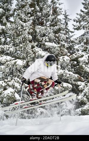 Männlicher Skifahrer in weißer Jacke und Helm Skifahren auf frischem Pulverschnee mit schönen verschneiten Bäumen im Hintergrund. Mann macht springen, während Sie hinunter verschneiten Hängen. Konzept des Wintersports Stockfoto