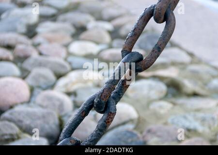 Alte geschmiedete rostige Kette mit abblätternder Farbe auf dem Hintergrund der Pflastersteine. Stockfoto