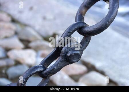 Alte geschmiedete rostige Kette mit abblätternder Farbe auf dem Hintergrund der Pflastersteine. Stockfoto