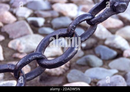 Alte geschmiedete rostige Kette mit abblätternder Farbe auf dem Hintergrund der Pflastersteine. Stockfoto