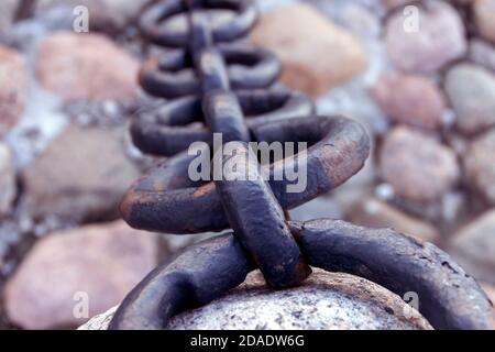 Alte geschmiedete rostige Kette mit abblätternder Farbe auf dem Hintergrund der Pflastersteine. Stockfoto