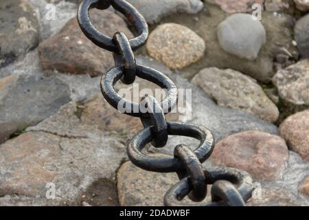 Alte geschmiedete rostige Kette mit abblätternder Farbe auf dem Hintergrund der Pflastersteine. Stockfoto