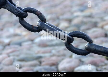 Alte geschmiedete rostige Kette mit abblätternder Farbe auf dem Hintergrund der Pflastersteine. Stockfoto