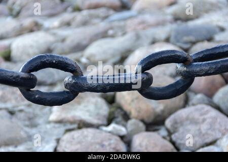 Alte geschmiedete rostige Kette mit abblätternder Farbe auf dem Hintergrund der Pflastersteine. Stockfoto