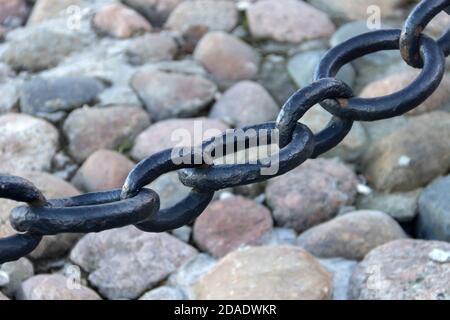 Alte geschmiedete rostige Kette mit abblätternder Farbe auf dem Hintergrund der Pflastersteine. Stockfoto