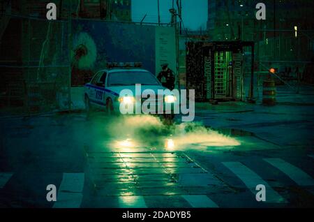 Polizeifahrzeug mit seinen Scheinwerfern werfen Licht auf Dampf Cominf der Kanalisation in Lower Manhattan, New York City, USA Stockfoto