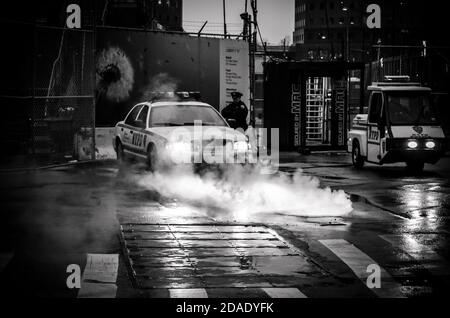 Schwarz-Weiß Foto eines Polizeifahrzeugs mit seinen Scheinwerfern Licht auf Dampf werfen Cominf der Kanalisation in Lower Manhattan, New York City, USA Stockfoto