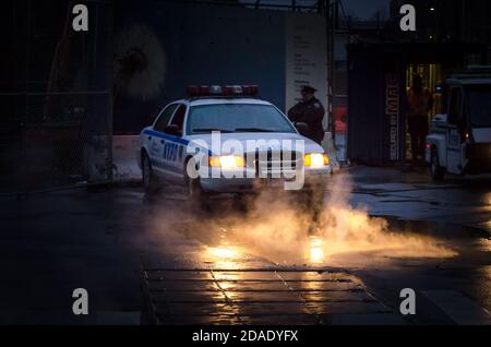 Polizeifahrzeug mit seinen Scheinwerfern werfen Licht auf Dampf Cominf der Kanalisation in Lower Manhattan, New York City, USA Stockfoto