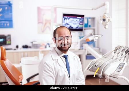 Selbstbewusster Zahnarzt in Stomatologie Schrank mit orangen Ausrüstung tragen Zahnuniform. Medizinische Fachkraft für Mundhygiene tragen Laborkittel Blick auf Kamera in der Zahnmedizin Büro. Stockfoto