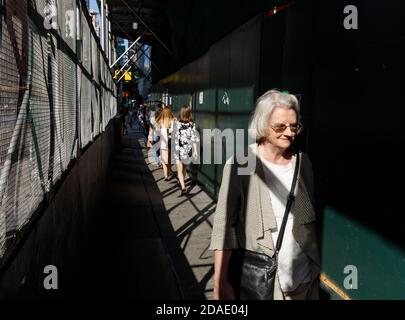 NEW YORK, USA - 17. Sep 2017: Manhattan Street scene. Reife grauhaarige Frau mit Brille auf Bürgersteig mit einem Schutzzaun in der Nähe Konstrukt zu gehen Stockfoto