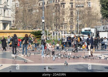 Barcelona, Spanien - 24. Feb 2020: Fußgänger füttern Tauben am sonnigen Nachmittag auf der Plaza de Catalunya Stockfoto