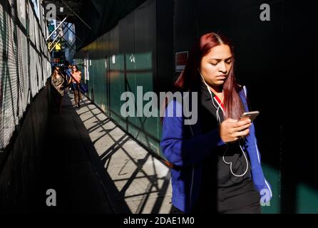 NEW YORK, USA - 17. Sep 2017: Manhattan Street scene. Junge Frau mit Handy läuft auf Bürgersteig mit einem Schutzzaun in der Nähe von Bauarbeiten Stockfoto