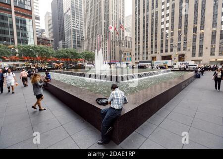 NEW YORK, USA - 18. Sep 2017: Manhattan Street scene. Amerikaner auf den Straßen von New York City. Ein Mann sitzt in der Nähe eines Brunnens an der 6th Avenue von Manhattan Stockfoto