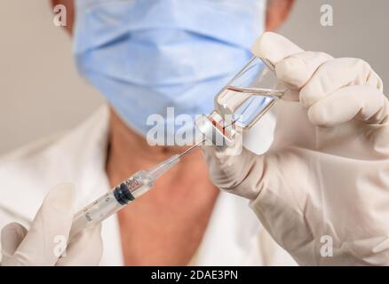 Nadel einer Spritze in einem Impfstoffbehälter. Die Hände sind mit Handschuhen geschützt Stockfoto