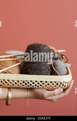 Nahaufnahme einer Frau, die den Korb mit Wolle und Stricknadeln hält Zum Stricken isoliert auf rosa Hintergrund arbeiten Stockfoto