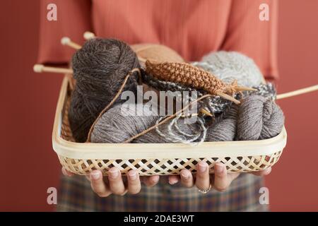 Nahaufnahme einer Frau, die den Korb mit Garn und Nadeln hält Ihre Hände isoliert auf rosa Hintergrund Stockfoto