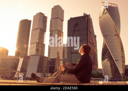 Moskau / Russland - 18. AUGUST 2018: Der Mann sitzt auf dem Hintergrund des Geschäftszentrums, in der Nähe von Bürogebäuden. Gläserne Wolkenkratzer an einem Abend. Firmenbus Stockfoto