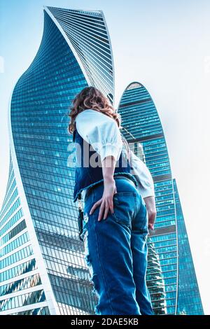 Moskau / Russland - 18. AUGUST 2018: Mädchenstand des Geschäftszentrums. Frau in Jeans in der Nähe von Bürogebäuden. Gläserne Wolkenkratzer an einem sonnigen Tag. Unternehmen Stockfoto