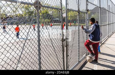 NEW YORK, USA - 28. Apr 2016: Jungs beobachten die Kinder beim Fußballspielen auf dem Kinderspielplatz in Brooklyn, New York City Stockfoto