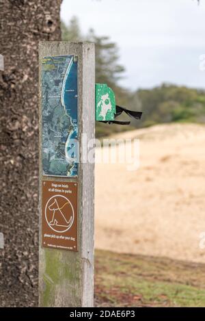 Ein Schild in der Größe eines Wegweisers mit einer Mini-Karte, eine Warnung an Besitzer, Hunde an der Leine zu halten und einen Hundekastenspender. Stockfoto